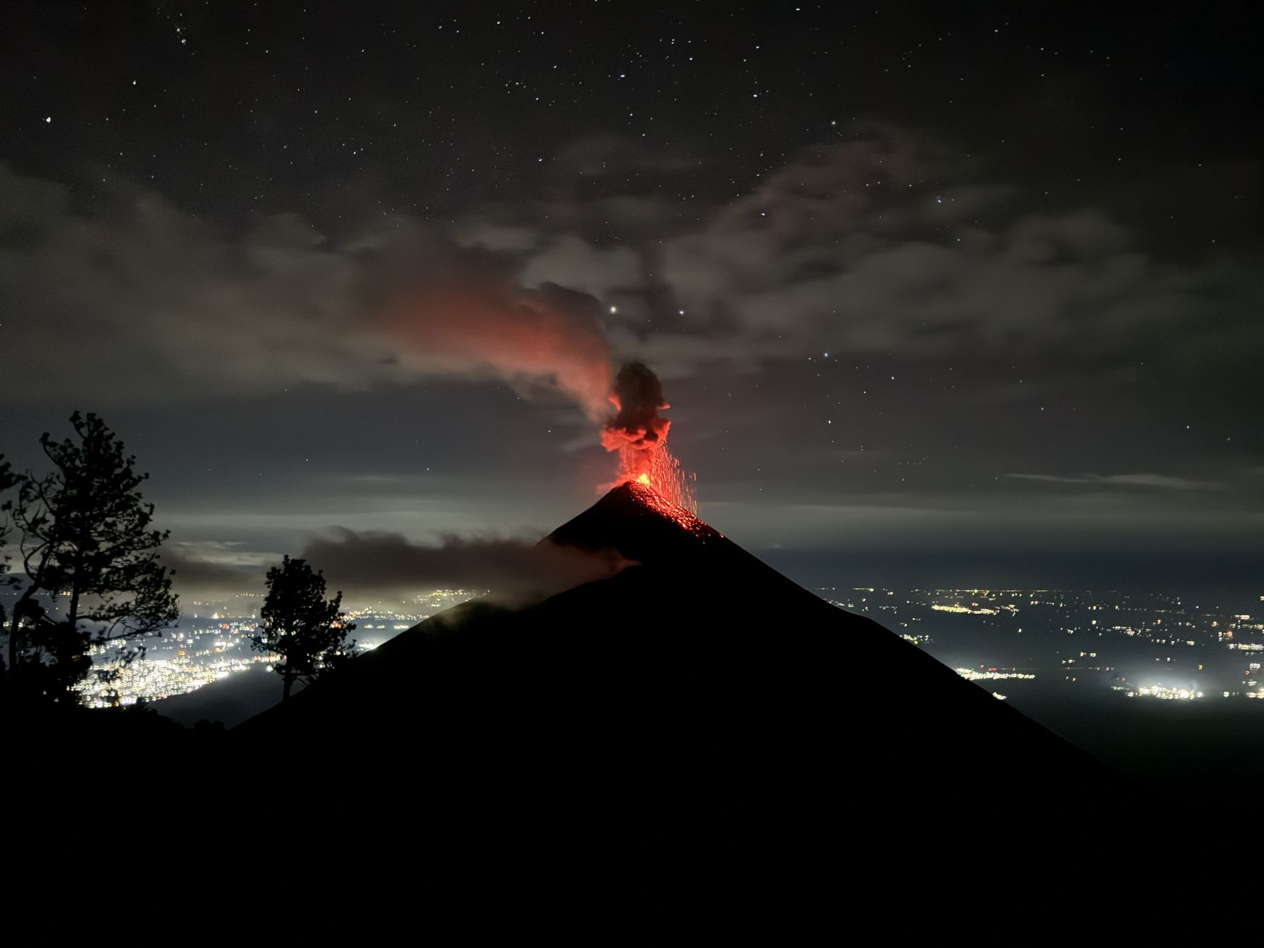 Volcán de Fuego erupting at night with lava and city lights below